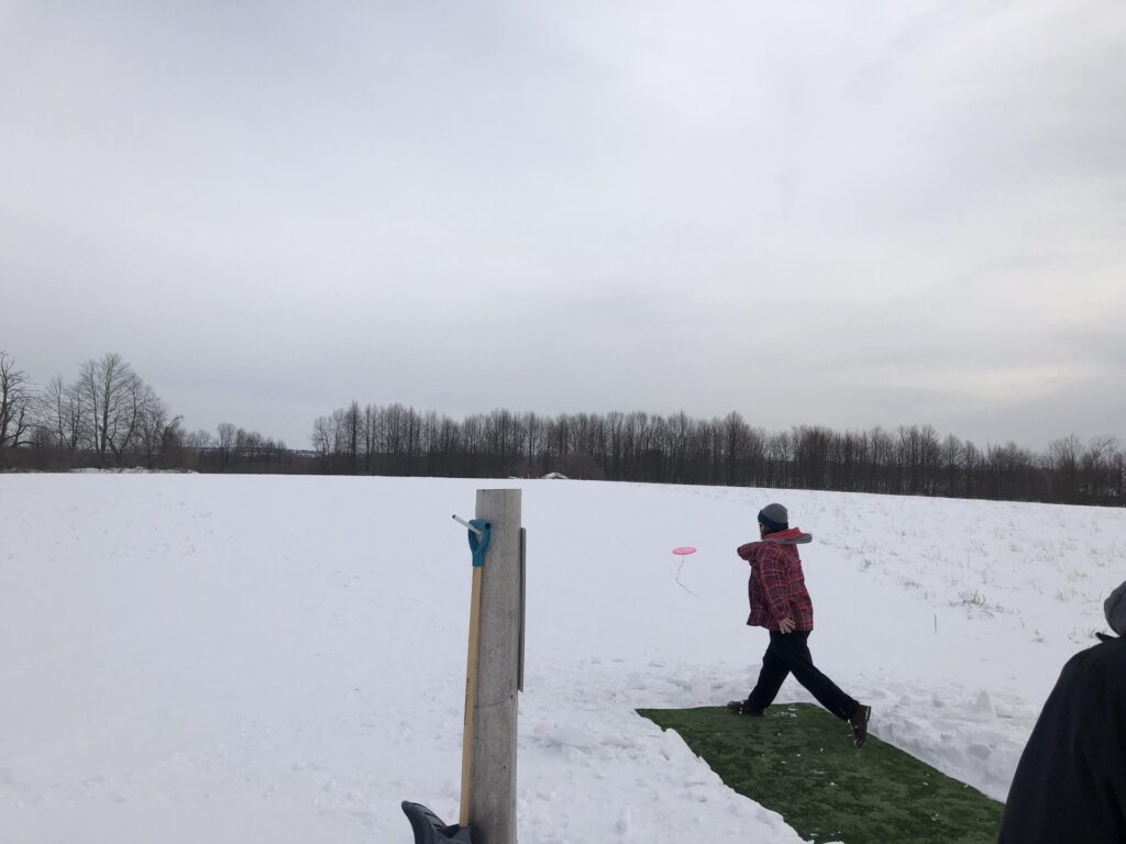 woman throwing a disc on a disc golf course in winter