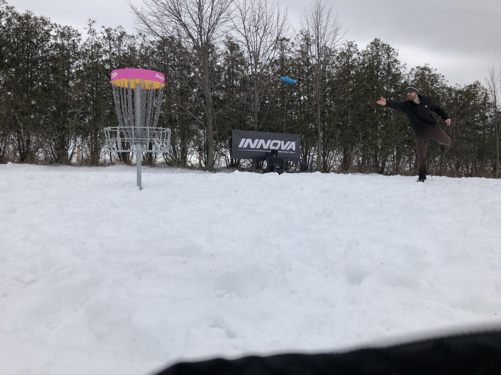 Man throwing a blue disc into a disc golf basket on a course in winter