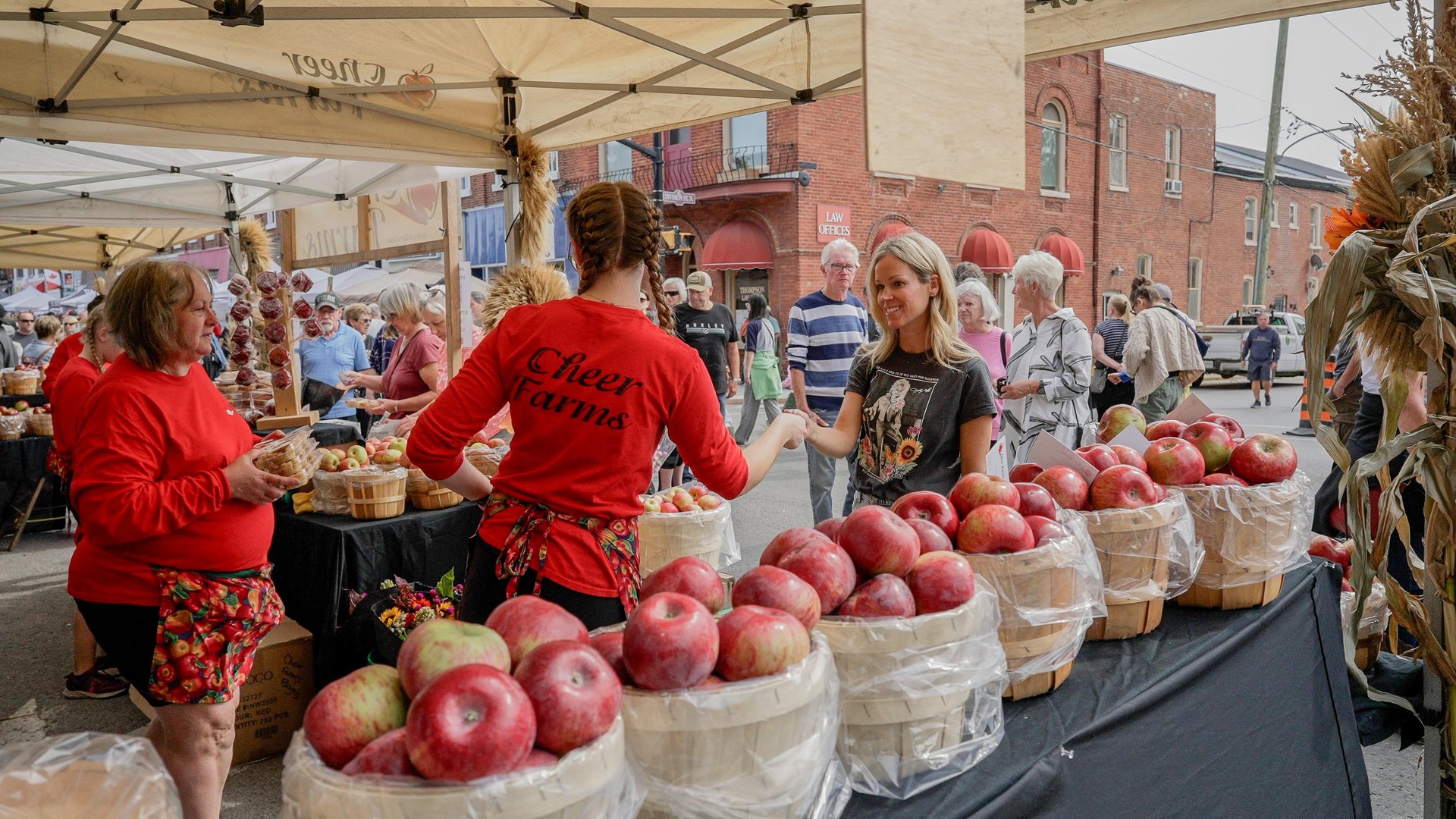 A vendor at a street festival with a row of apple bushels on the table