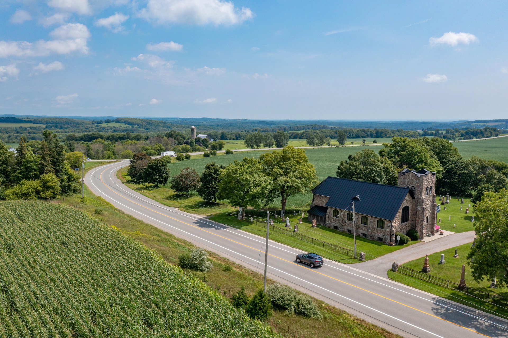 Drone view of car driving past church on a country road