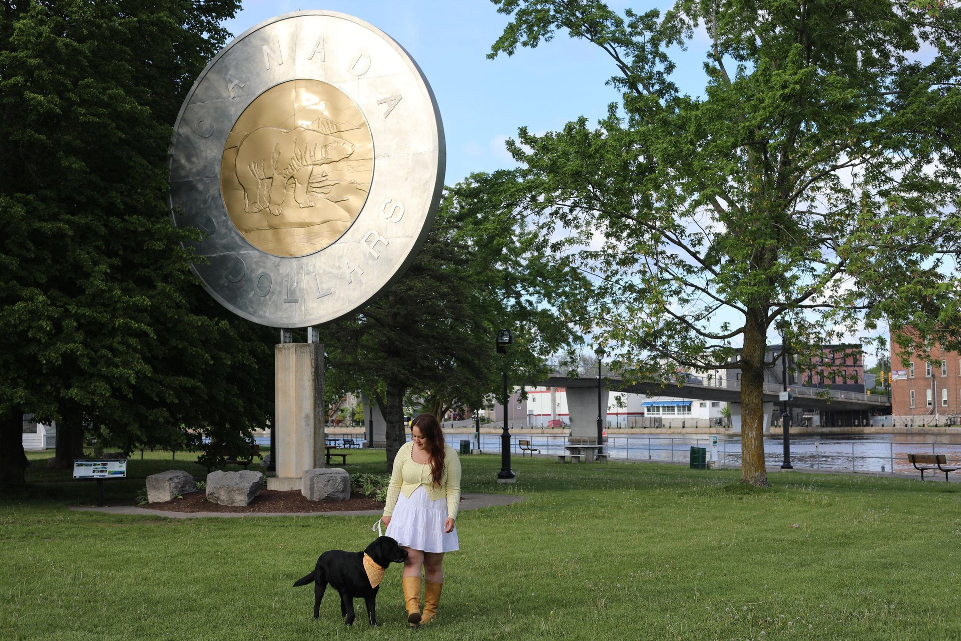 Woman and black dog walking in front of giant $2 coin