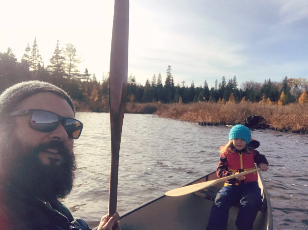 Selfie of father and child in a canoe holding oars on the lake in fall