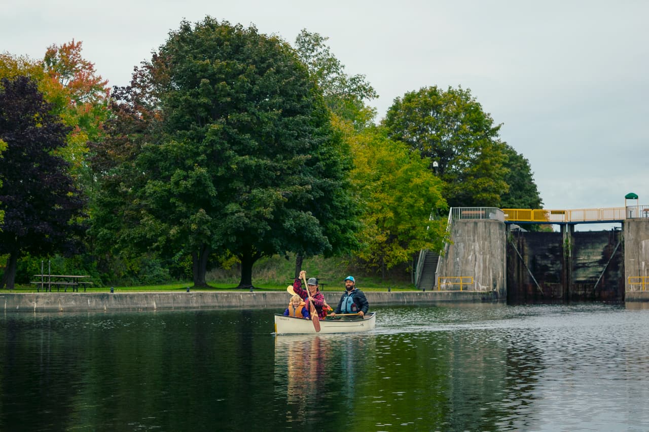 Family in a white canoe paddling away from a set of locks on a river in the fall.
