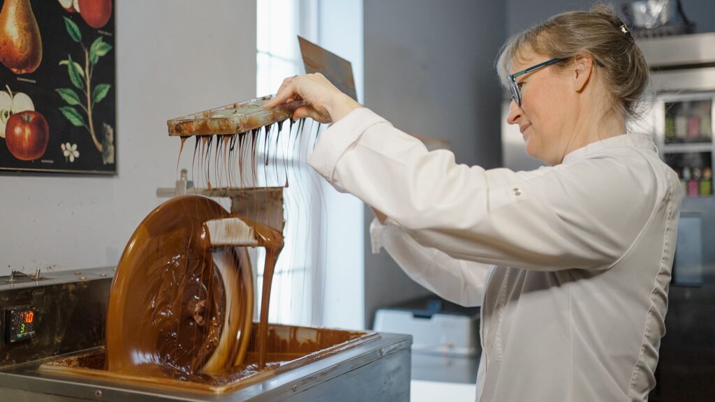 Woman making chocolate wearing a white coat.