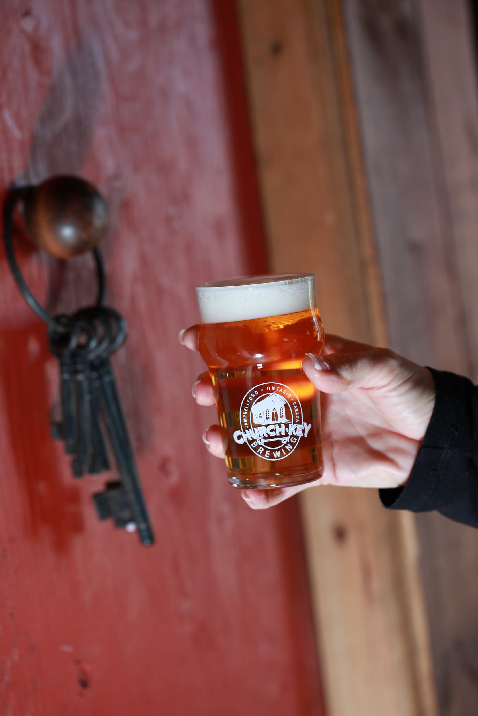 Hand holding a glass of Church Key Beer in front of a vintage door