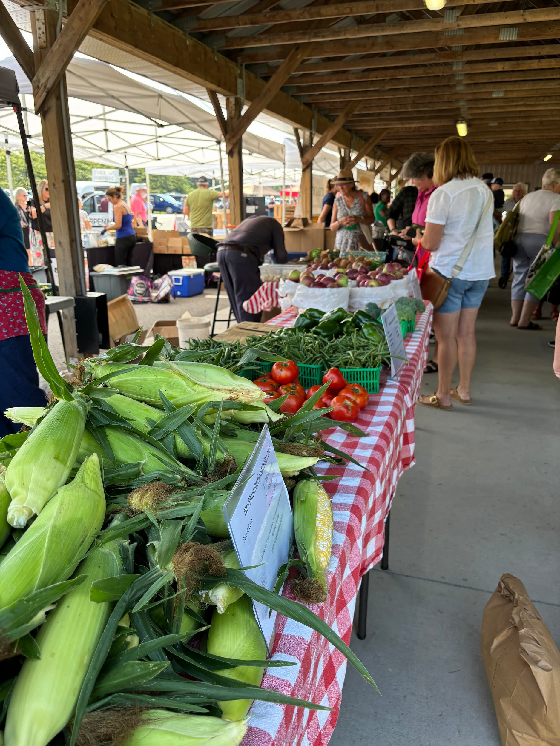 Row of merchant tables at a farmers' market in a covered pavilion.