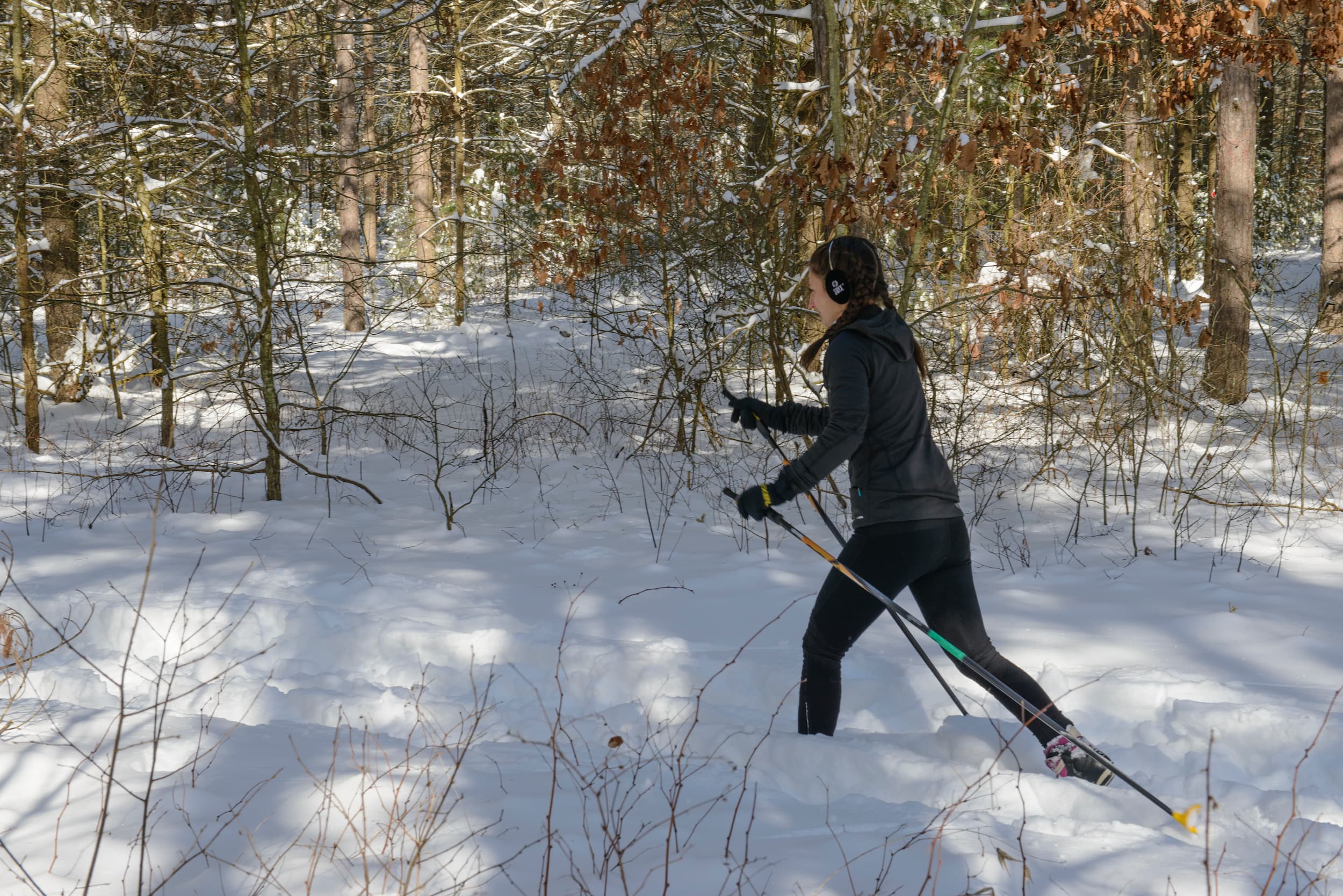 Person wearing all black cross-country skiing in a wooded area.