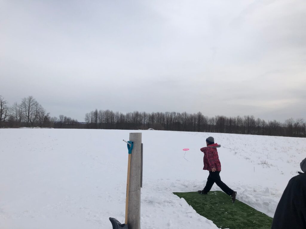 Person throwing a disc from a tee at a disc golf course in winter.