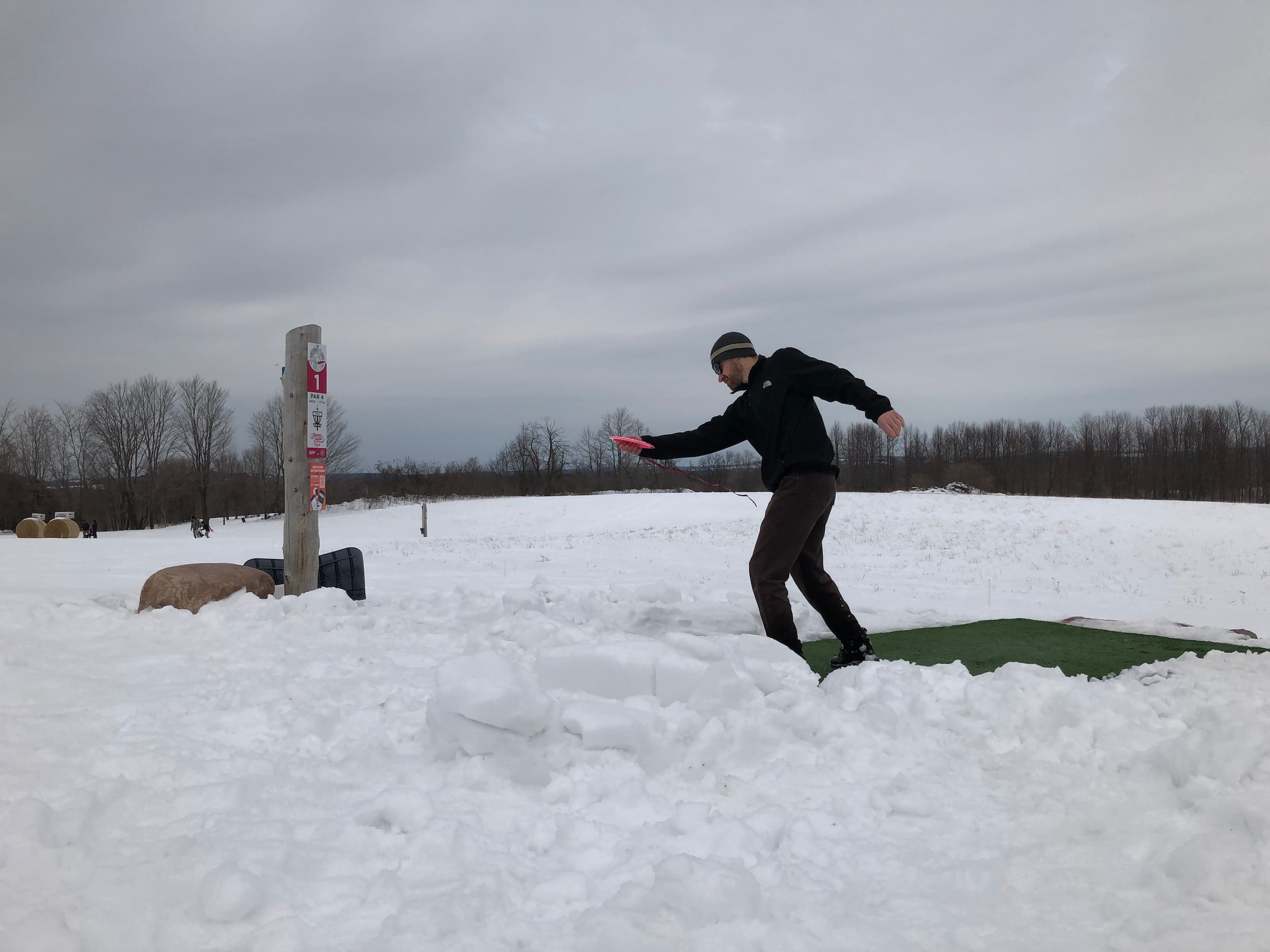 Man throwing a disc towards a disc golf basket in winter