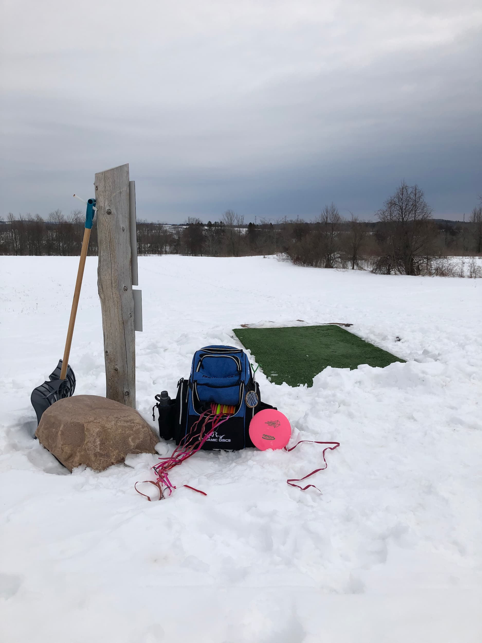 Disc golf bag sitting beside a disc golf tee in winter.