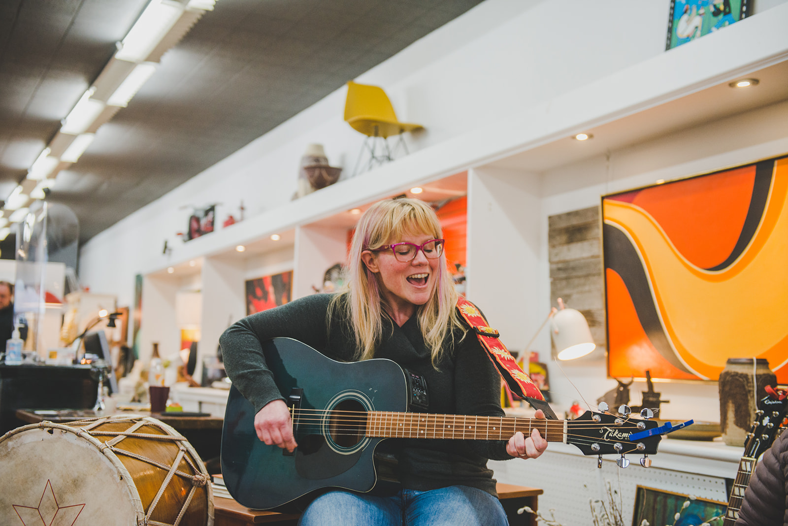 Woman singing and playing guitar in a colourful retail store