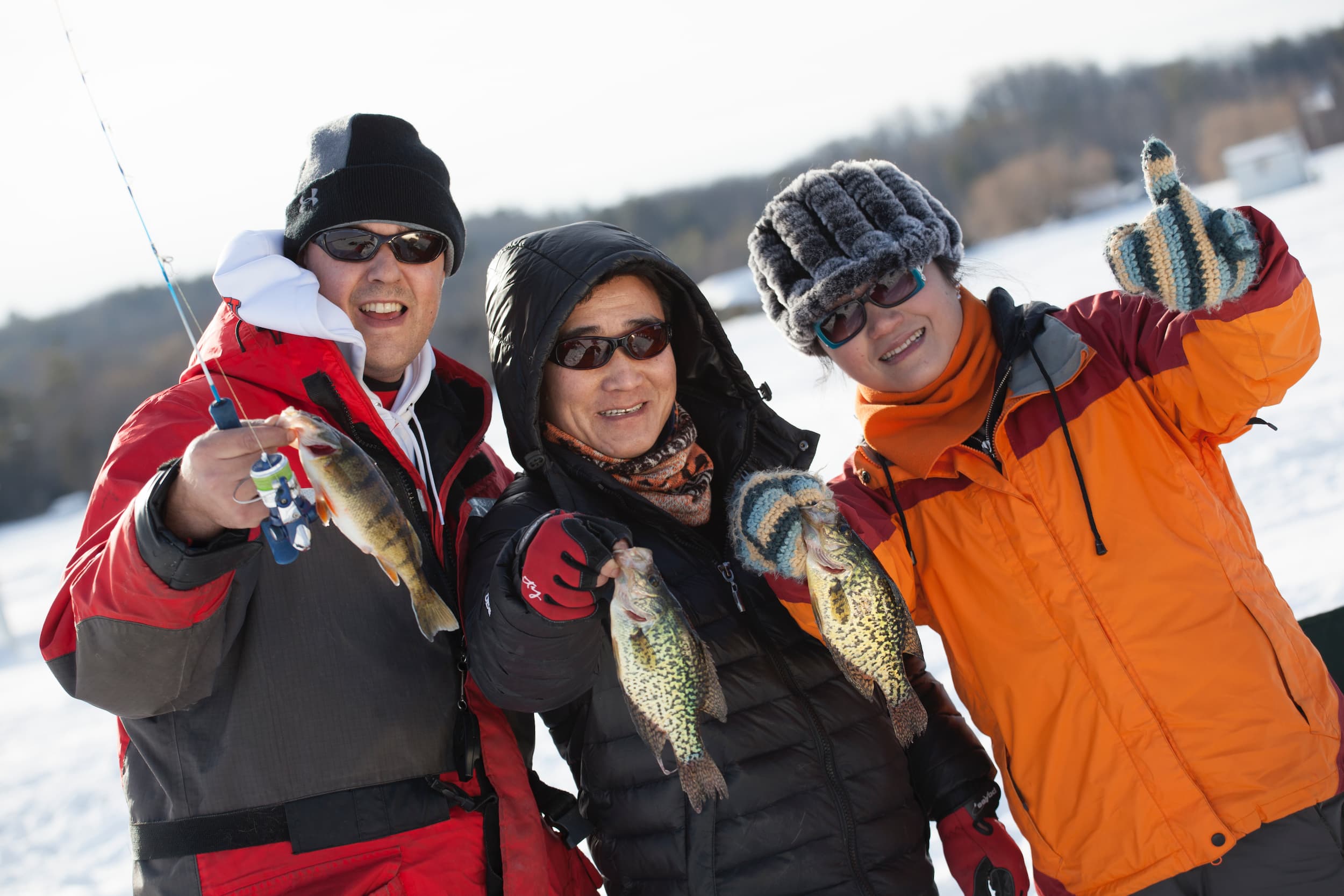 Group of three people dressed in winter great holding up pan fish caught while ice fishing on Rice Lake.