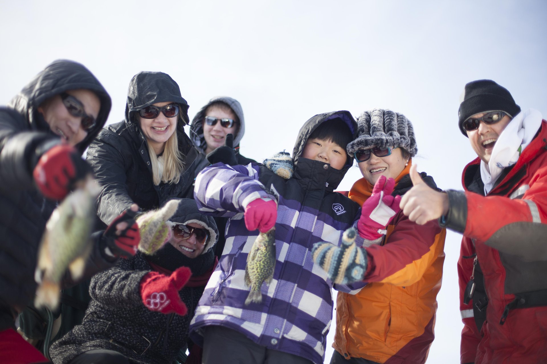 Group of people in winter clothing holding small panfish caught while ice fishing