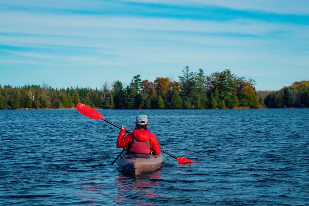 Person wearing a red coat in a kayak with red paddles.