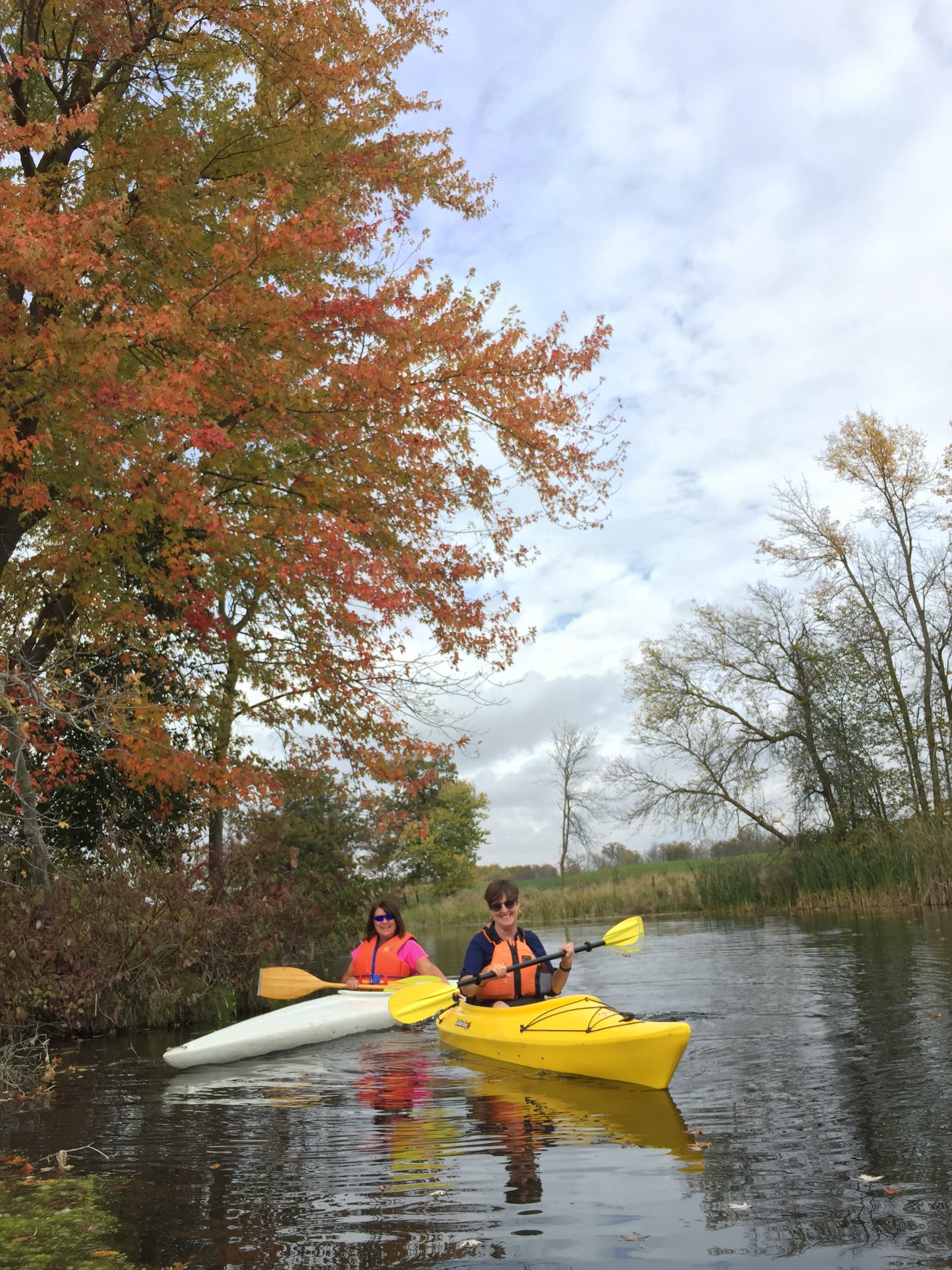 2 women in kayaks paddling a river in the fall