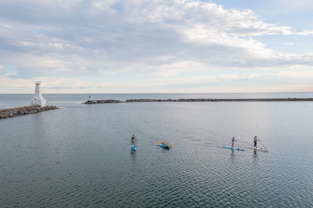 Drone view of a family paddle boarding and kayaking in a harbour with a lighthouse in the background.