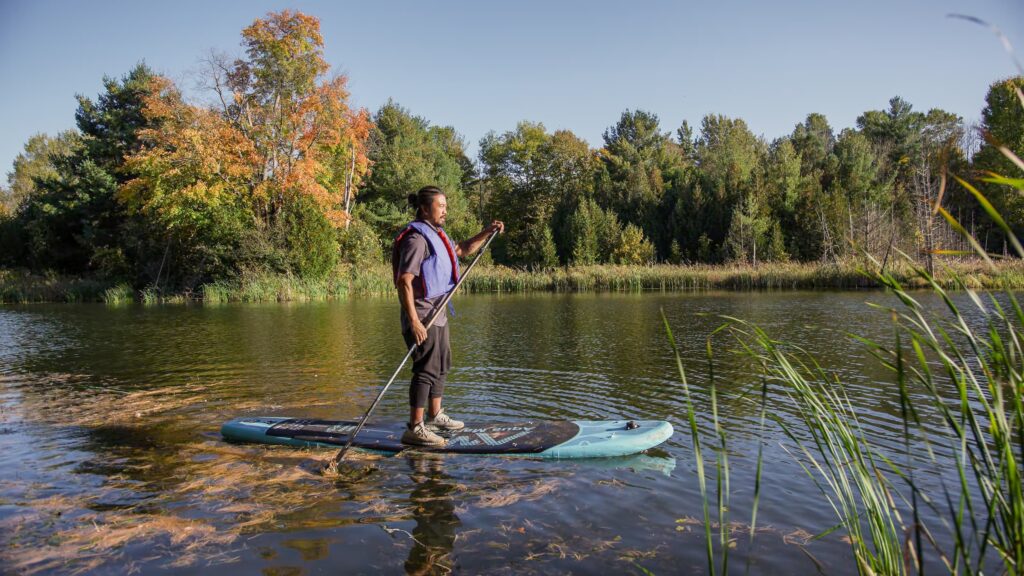 Man standing on a paddle board on a small body of water in fall