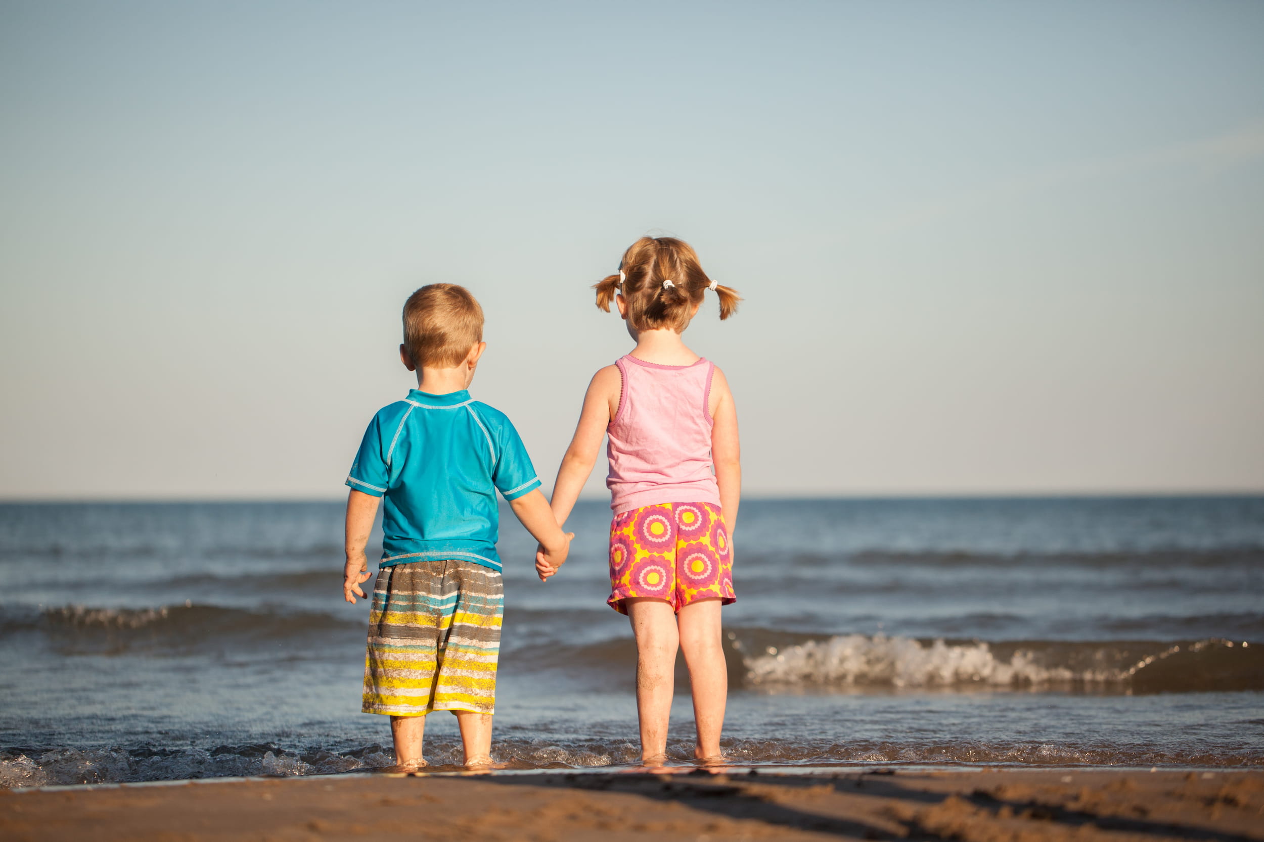 Young children holding hands standing at the edge of the water at Port Hope Beach