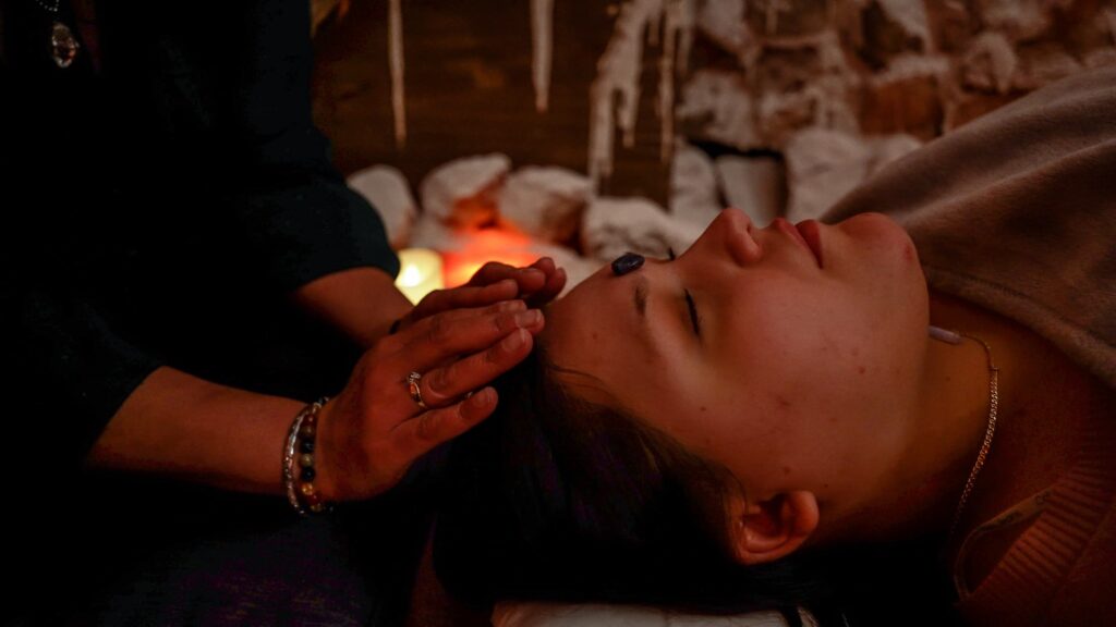 Woman laying on the floor in a salt cave with her eyes clothes. A therapist's hands are on her forehead.