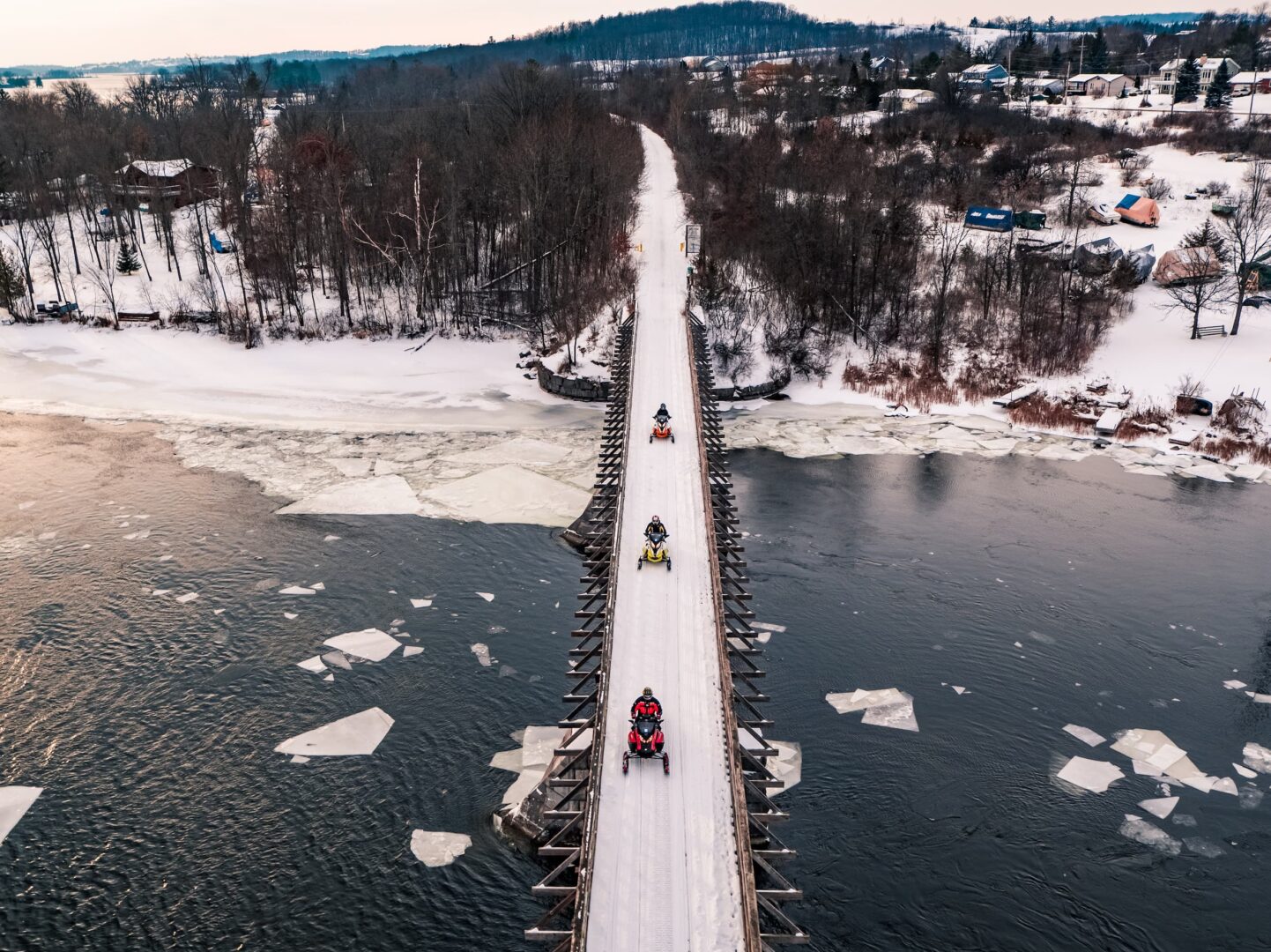 Drone view of three snowmobiles driving on snow-covered bridge over Trent River in Hastings.