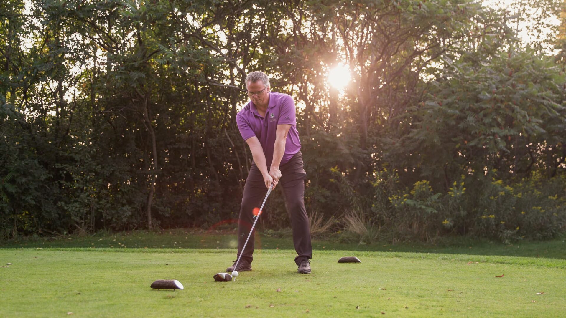 Man getting ready to hit a shot on a golf course at dusk.
