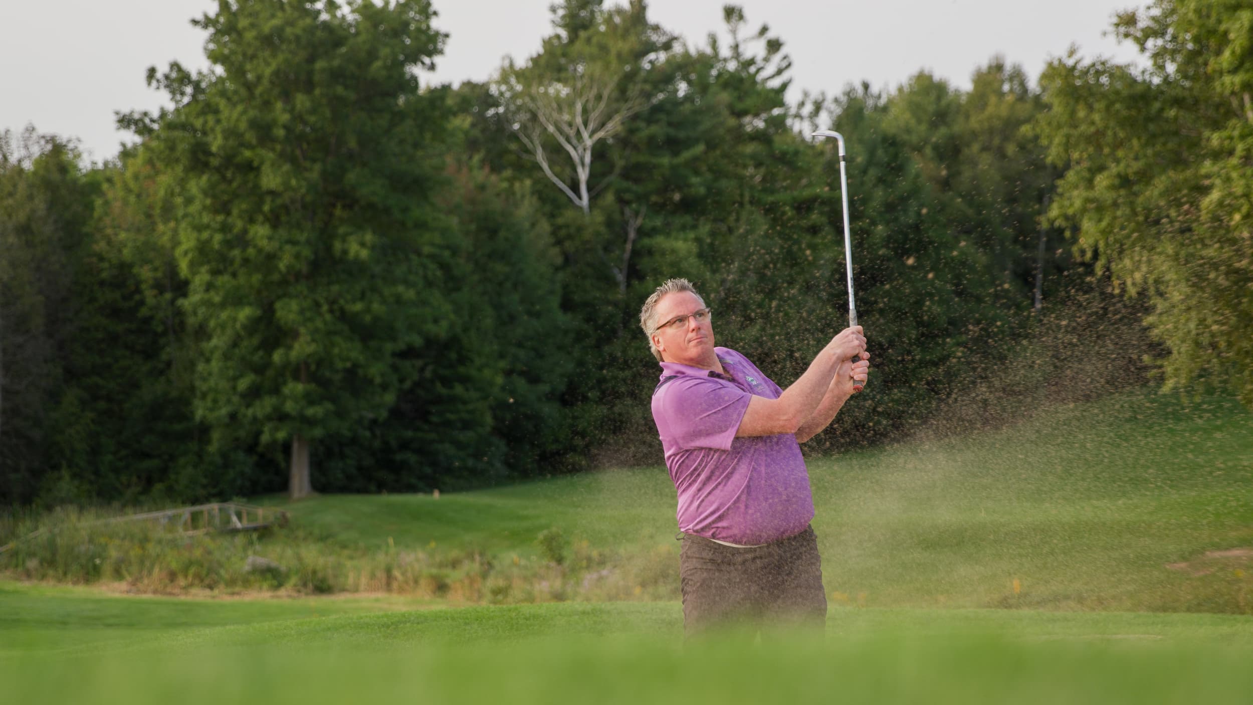 Man hitting a ball out of a sand trap.