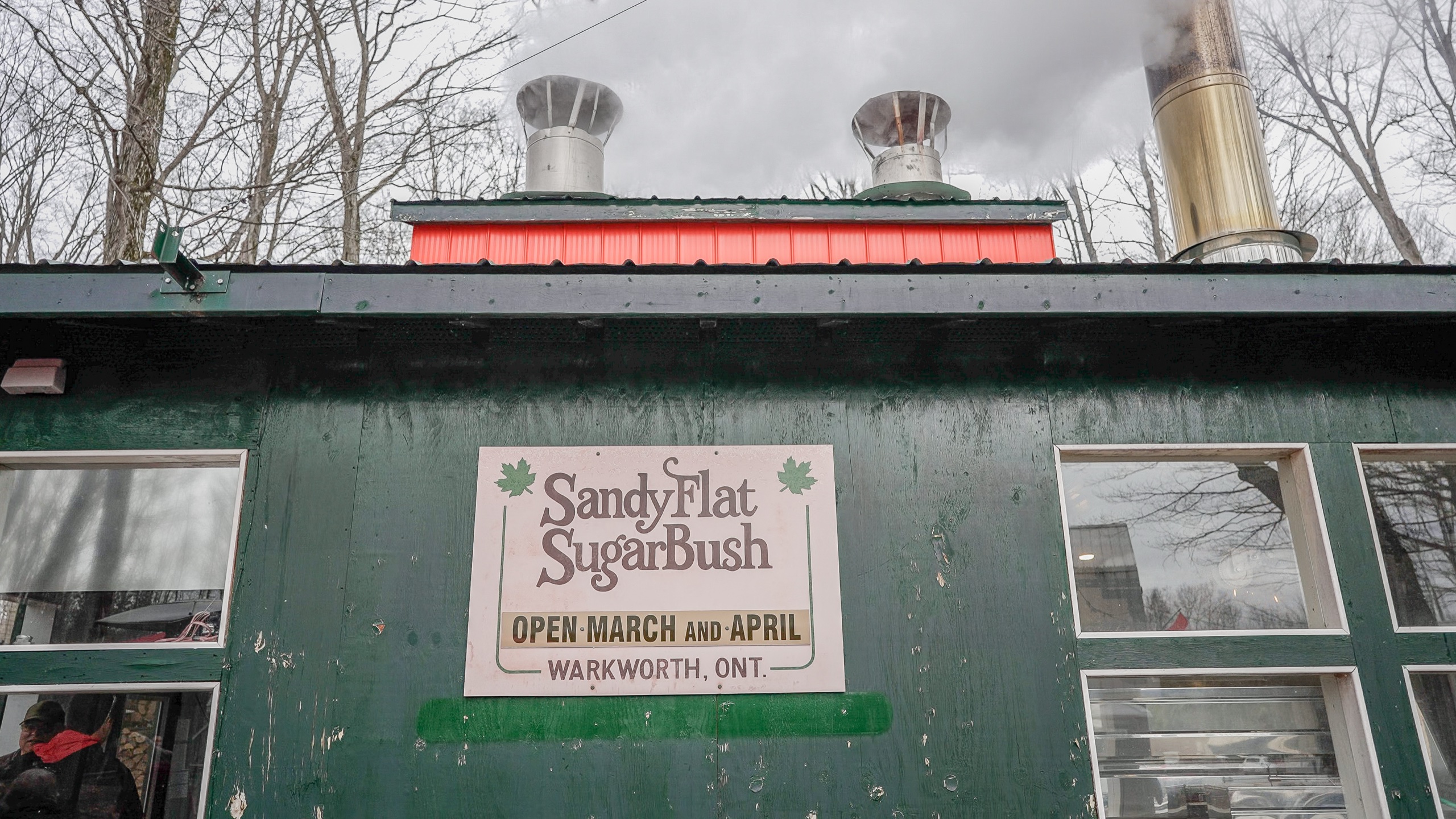 Photo of sign on the outside of the Sandy Flat Sugar Bush. Sign reads "Sandy Flat Sugar Bush. Open March and April. Warkworth, Ont."