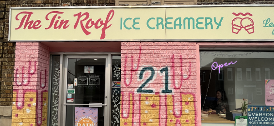 A brick building painted pink and tan with a white sign with pink and blue writing.