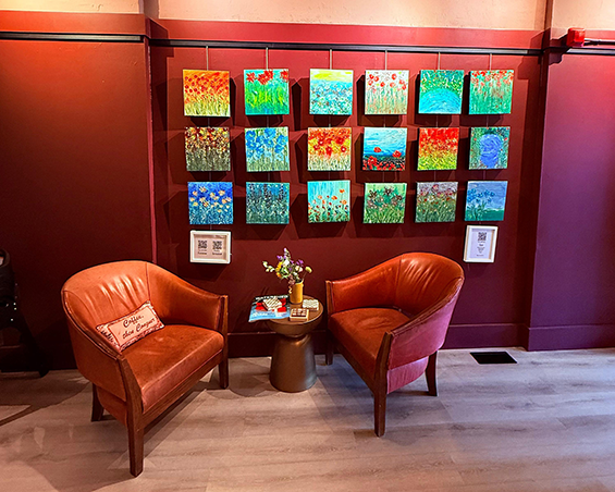 2 leather tub chairs sitting in front of a collection of art hanging on a coffee shop wall