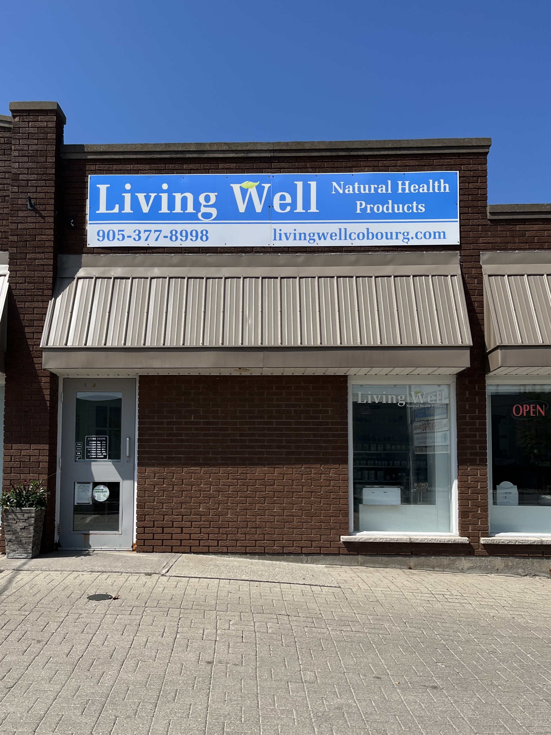 Photo of Living Well Natural Health Products store front. Photo features a photo of sign above the entrance. Sign reads "Living Well Natural Health Products. 905-377-8998. livingwellcobourg.com."