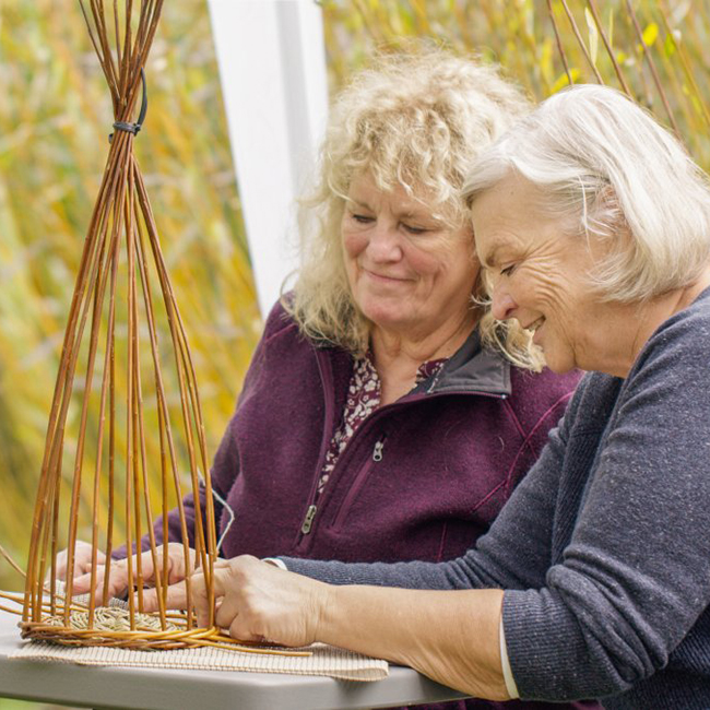 2 women weaving into wicker.