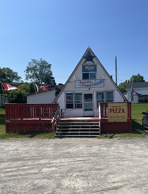 Triangular shaped building with a red deck in front with signs on the front.