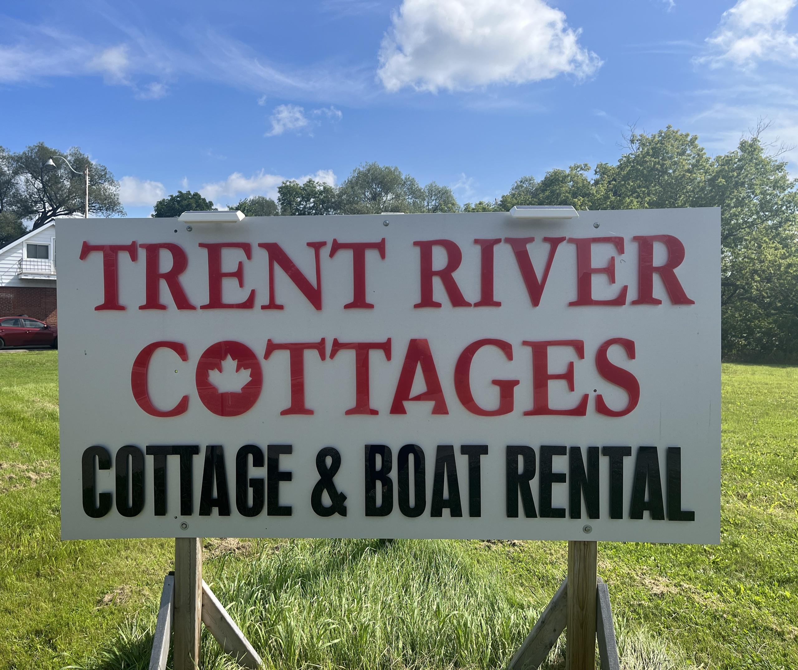 White sign reading "Trent River Cottages: Cottage and Boat Rental" in red text.