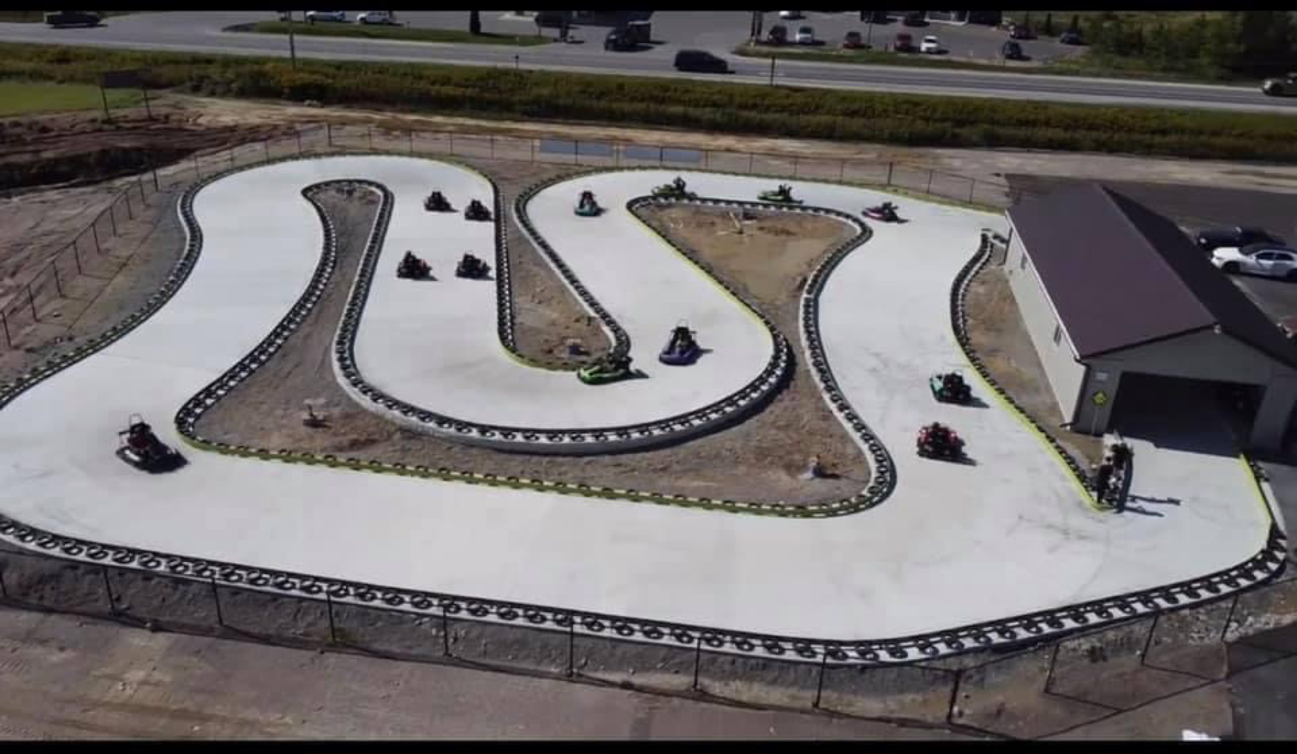 Windinng racetrack with go karts driving on it, alongside a highway
