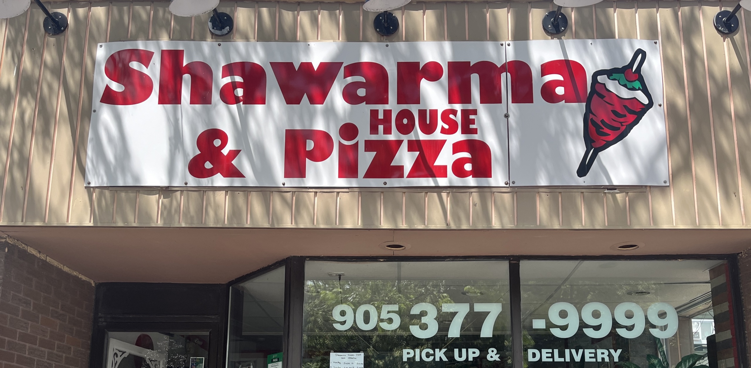 Photo of Shawarma House & Pizza store front. Sign above entrance reads "Shawarma House & Pizza. 905-377-9999. Pick up & delivery."