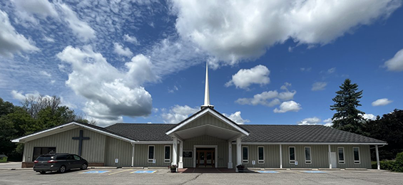 Long white building with a black roof and a tall white cross.