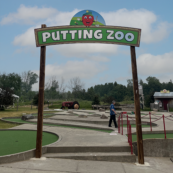 Mini-put course with a wooden and green sign with white writing in front.