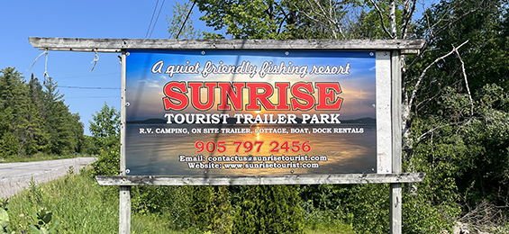 Sign with a sunset background and white and red writing.