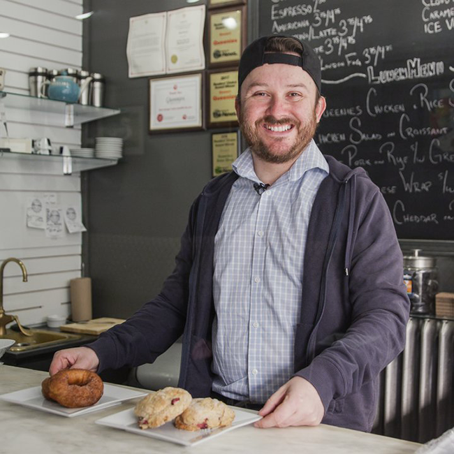 Man smiling holding 2 plates of turnovers and croissants.
