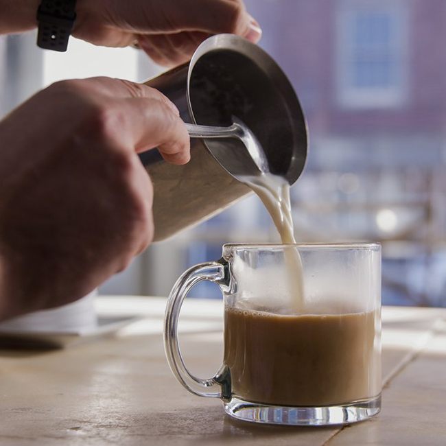 Person making a latte in a glass mug.
