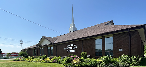Dark brown brick building surrounded by flower beds with a tall cross on top of the building.