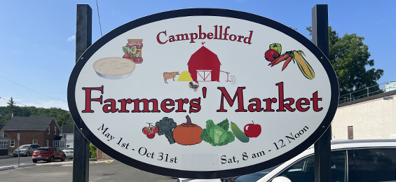 White sign with red writing and vegetables, preserves and a barn on it.