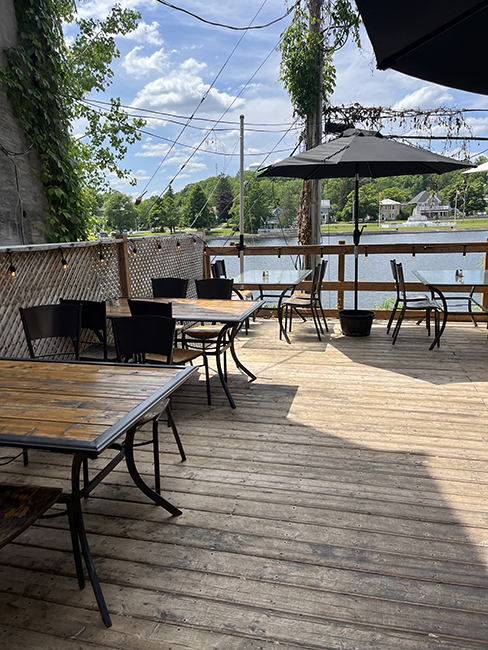Wooden patio with tables and chairs overlooking river.