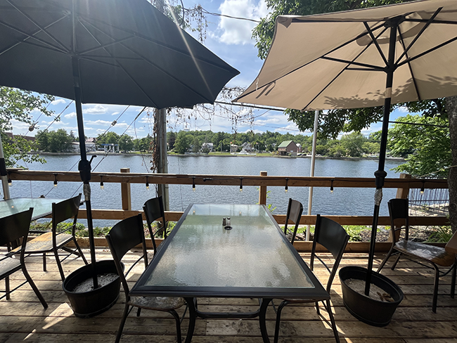 Wooden patio with tables and chairs overlooking river.