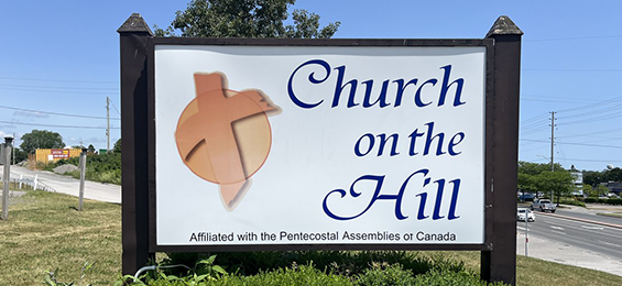 White sign with bule writing and an orange circle logo with a cross.