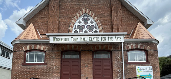 Large brick building with 2 identical red doors and a stained glass window.