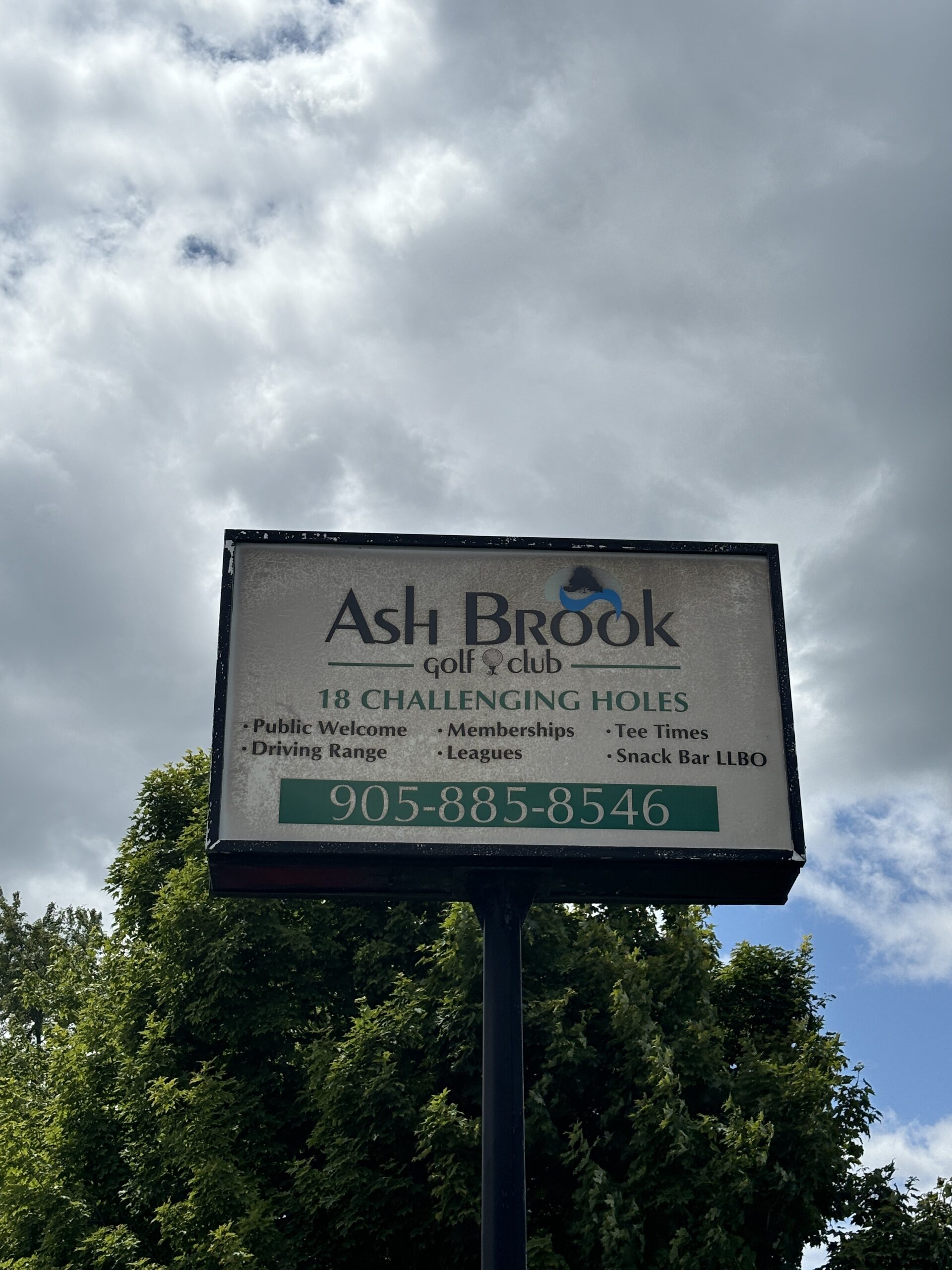 Photo of Ash Brook Gold Club sign. Sign reads "Ash Brook Golf Club. 18 Challenging Holes. Public welcome, memberships, tee times, driving range, leagues, snack bar LLBO. 9058858546."
