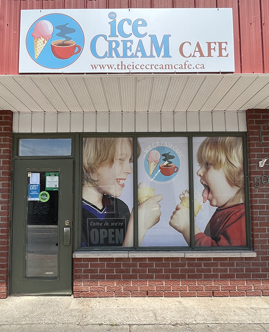 Red brick storefront with a mural in the window of 2 kids eating ice cream and a white sign above with blue and red writiing.