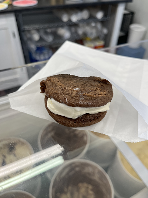 Vanilla ice cream between 2 chocolate cookies in a white paper bag.