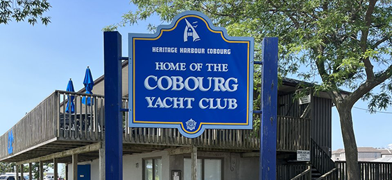 Blue city sign with white writing in front of a building with a large deck.